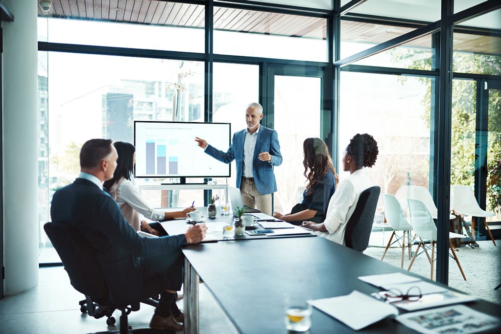 A meeting is taking place in an office. A gentleman presents the successes of the good cooperation. The picture symbolizes the partnership between MBI and HERE Technologies.