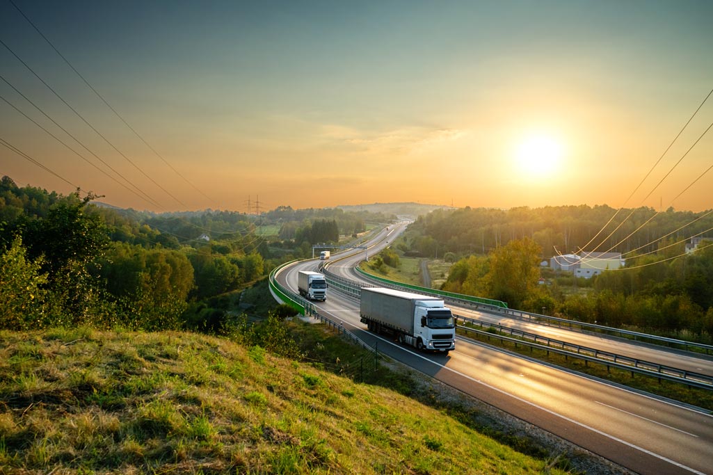 LKWs fahren auf einer Straße, über der Stromleitungen kreuzen. Die Elektrifizierung der Logistikbranche ist ein Thema des Logistic Summits 2023.