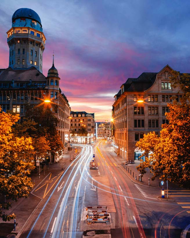 Visitors stream from one place to another in Zurich. You can see trails of light in the twilight.