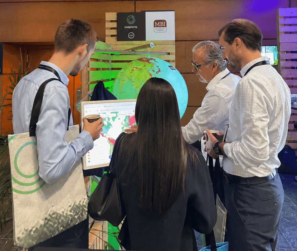 Visitors discussing geopolitical risk, supply chain resilience and sustainability with the MBI team at the Sustainability osapiens Summit 2026 booth